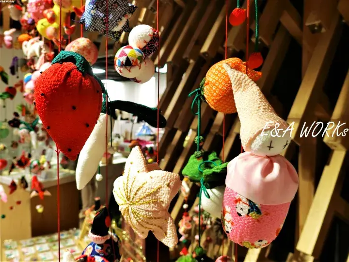Colorful handmade crochet ornaments including a strawberry, starfish, and cupcake hanging from red strings at E&A WORKS.