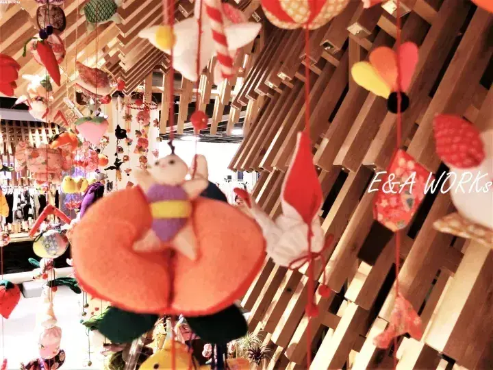 木製の梁にカラフルな手作りの布製オーナメントが吊るされた店内の風景。オレンジのスライスに乗ったウサギの飾りが目立つ。