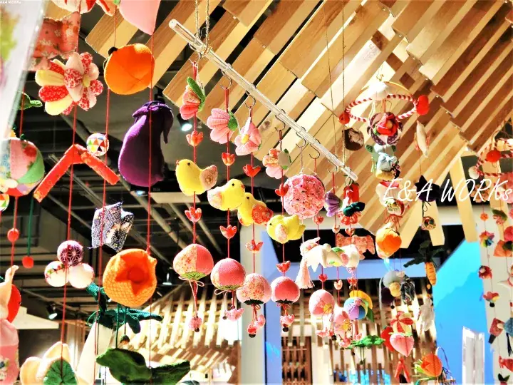Colorful handmade fabric ornaments hanging from wooden beams at a market stall.
