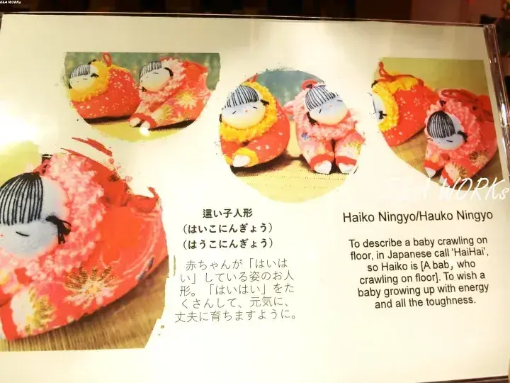 赤ちゃんの健康な成長を願う「這い子人形」の展示と、その意味を説明する日本語・英語のテキスト。