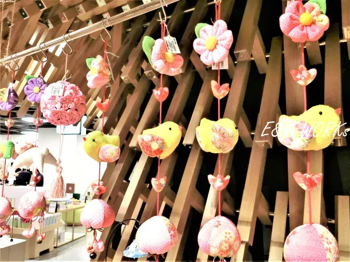 Colorful handmade fabric wind chimes hanging from wooden beams in a shop display.