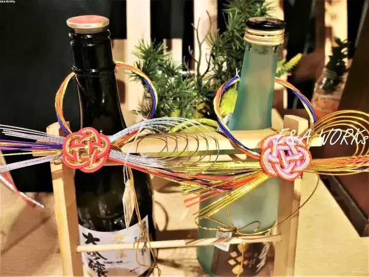 色とりどりの日本の伝統的な紐と結びで飾られた木製のケースに入った日本酒のボトル2本。