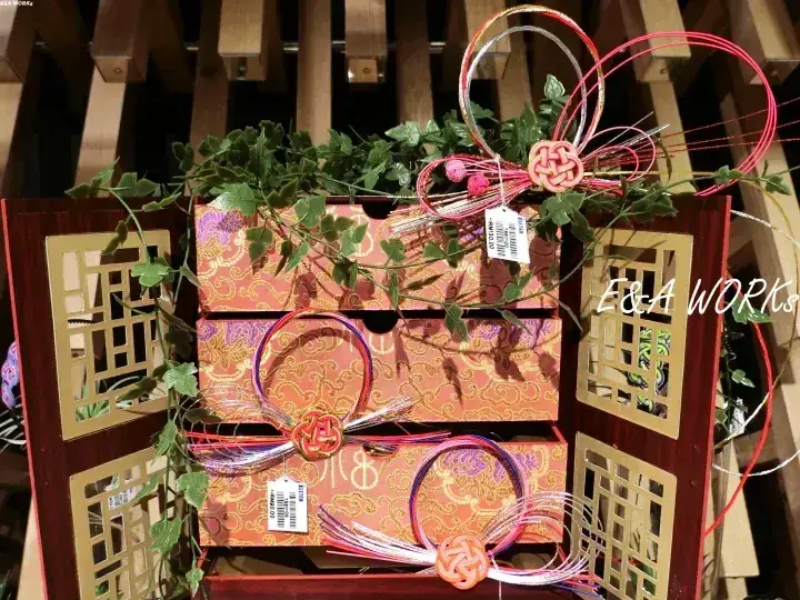 金色の模様が入った木製の箱に、カラフルなリボンや結び目、緑のアイビーが飾られた装飾品。
