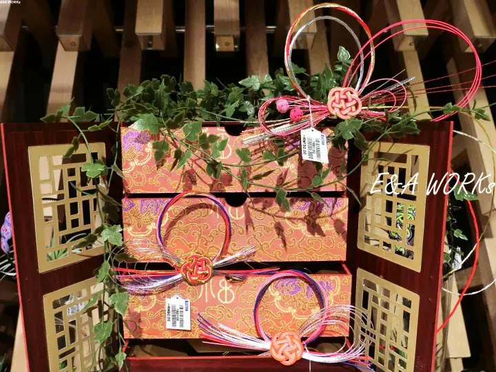 Decorative wooden boxes with intricate gold patterns, adorned with colorful ribbons, knots, and green ivy.
