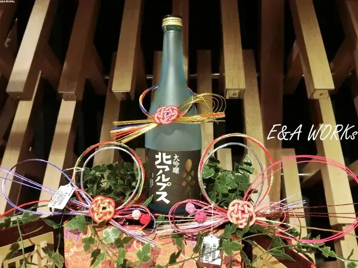 木製の棚に飾られた北アルプスの日本酒と装飾紐。