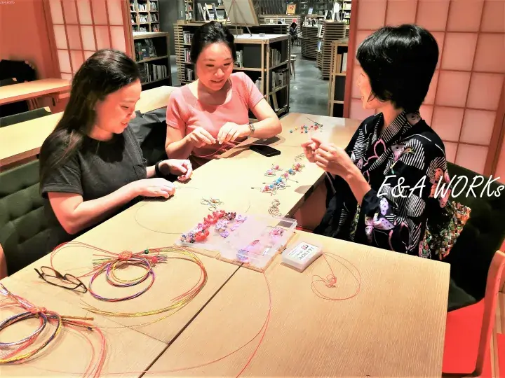 Three women crafting colorful beaded bracelets at a table in a bookstore during an E&A WORKS workshop.