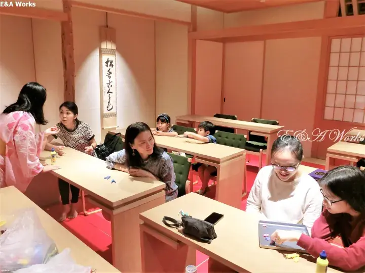 Guests and children participate in a traditional Japanese craft workshop inside a room with tatami mats and wooden furniture.