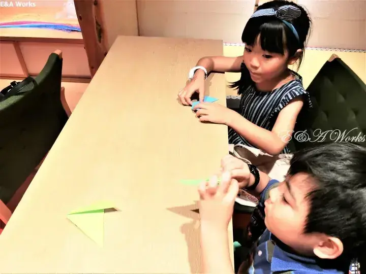 兩個孩子在明亮的室內木桌旁摺疊彩色摺紙。