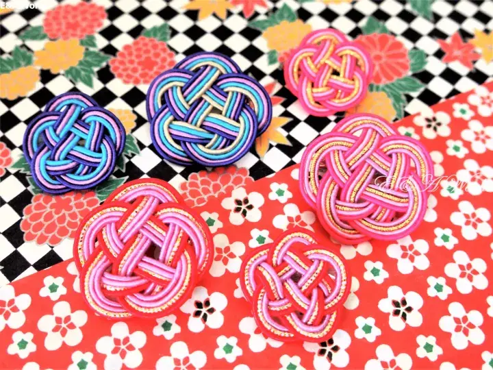 Colorful handmade Japanese knot ornaments displayed on a black and white checkered background and a red floral patterned surface.