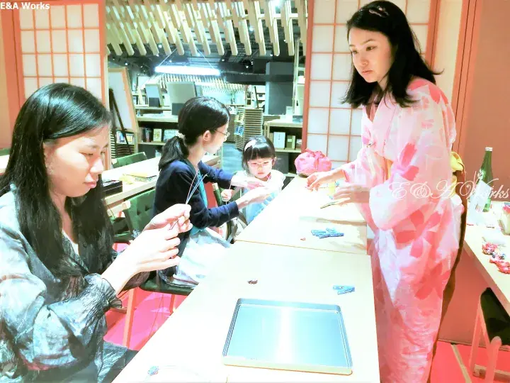 Women in kimonos and casual wear participate in a traditional craft activity at a Japanese-style venue.