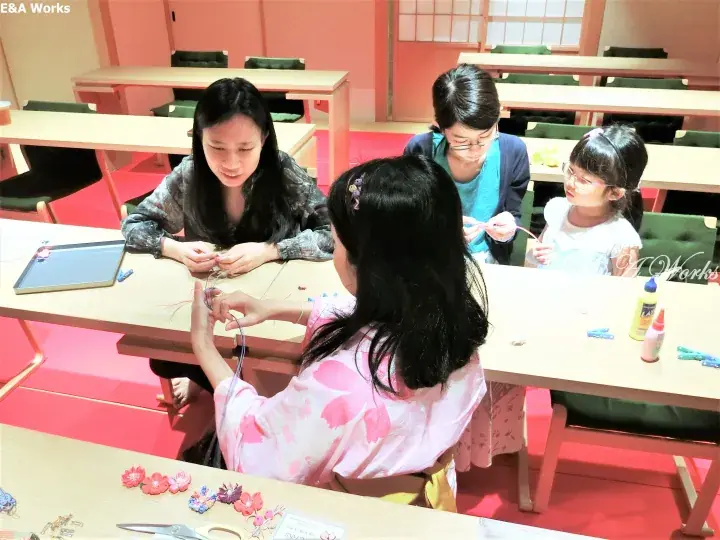 Participants engage in a traditional Japanese craft activity at a workshop table in a bright, modern studio space.