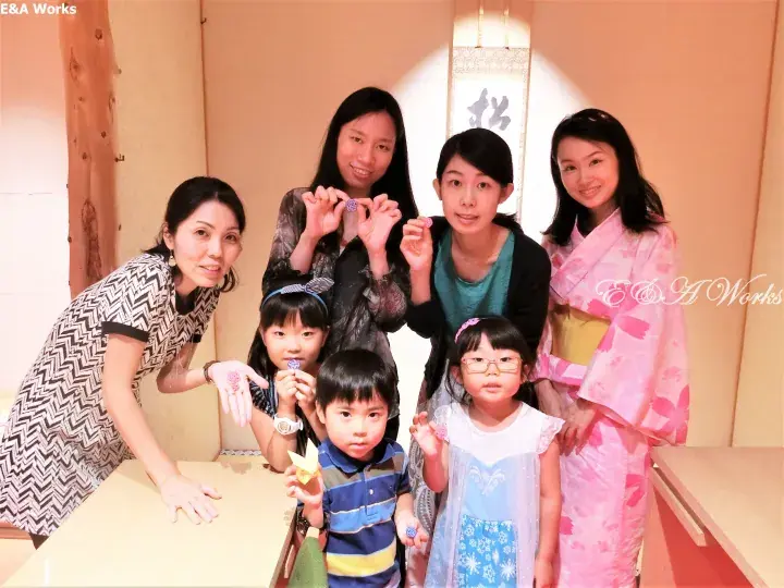 A group of adults and children posing together in a traditional Japanese room, with one woman wearing a pink kimono.