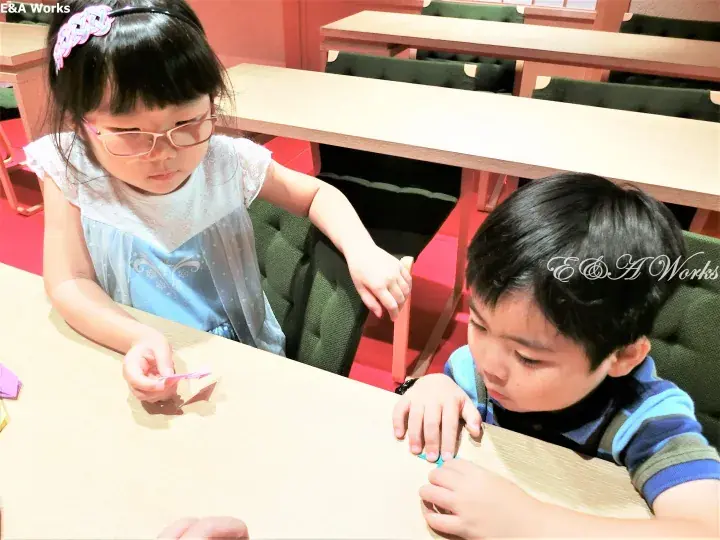 Two young children sitting at a table in a classroom, focused on playing with small objects.