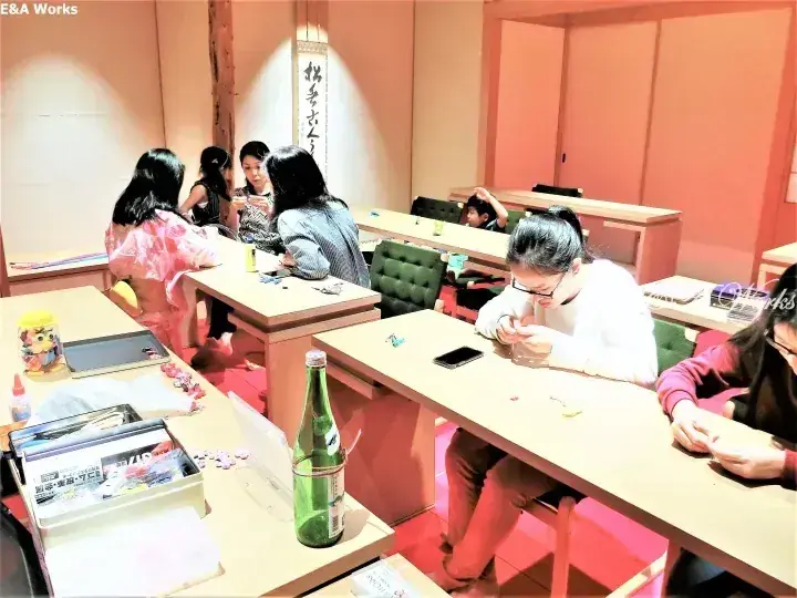 在溫暖的木質室內空間中,客人們正在參加手工活動,桌上擺放著桌椅和綠色瓶子。