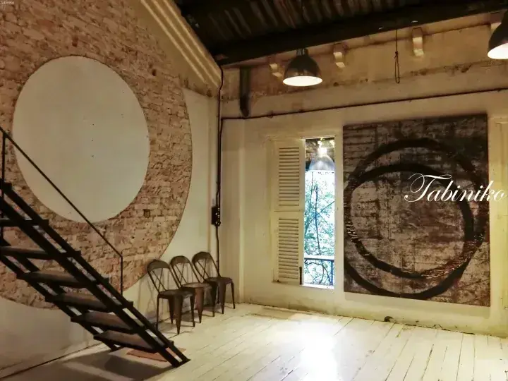 Industrial loft interior with exposed brick wall, spiral staircase, and large circular artwork in a bright room.