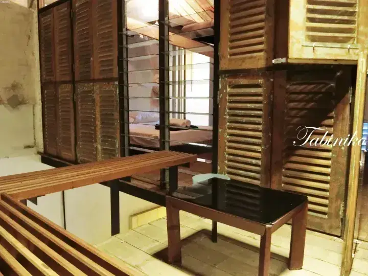 Interior of Tabinika hostel featuring wooden bunk beds with louvered doors and a small table in a rustic room.