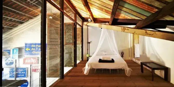 A rustic bedroom with a canopy bed, wooden beams, and glass walls showing street signs outside.