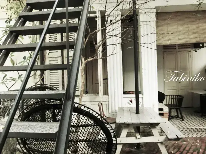 Outdoor patio with a black metal staircase, wooden picnic table, and wicker chairs at Tabiniko cafe.
