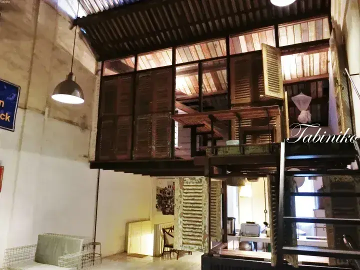 Interior view of Tabiniko featuring a suspended wooden structure with louvered shutters and industrial pendant lighting.