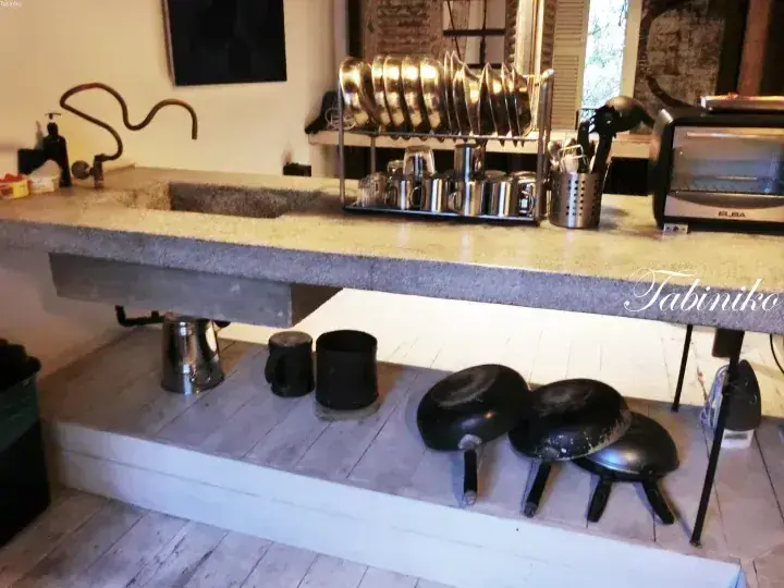 Industrial kitchen with concrete countertop, dish rack, and pots stored on a lower wooden shelf.