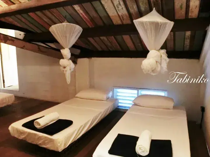 Two single beds with mosquito nets in a rustic room at Tabiniko, featuring wooden beams and a low ceiling.
