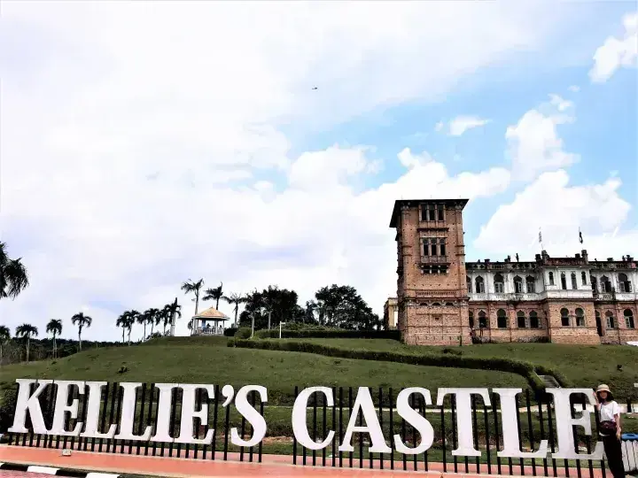 Kellie’s Castle in Ipoh, Malaysia, featuring its iconic unfinished brick tower and large white sign on a grassy hill.
