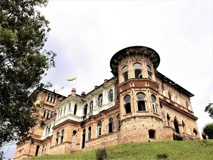 A historic brick building with a distinctive round tower and arched windows, set on a grassy hill under a cloudy sky.