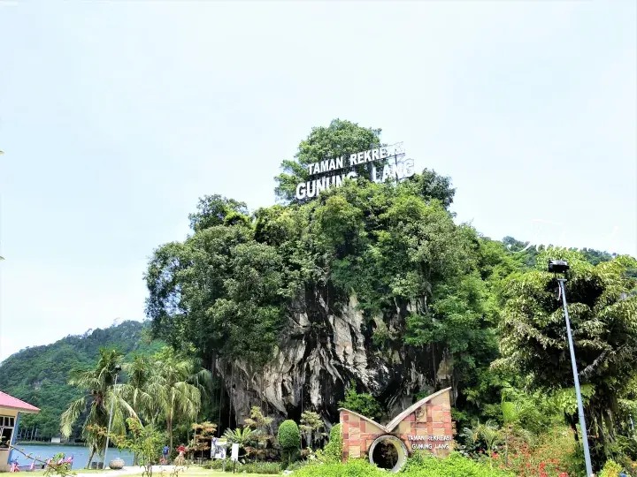 緑豊かな丘に「Taman Rekreasi Gunung Lang」の看板があり、その下には蝶の形をした入口構造物がある。