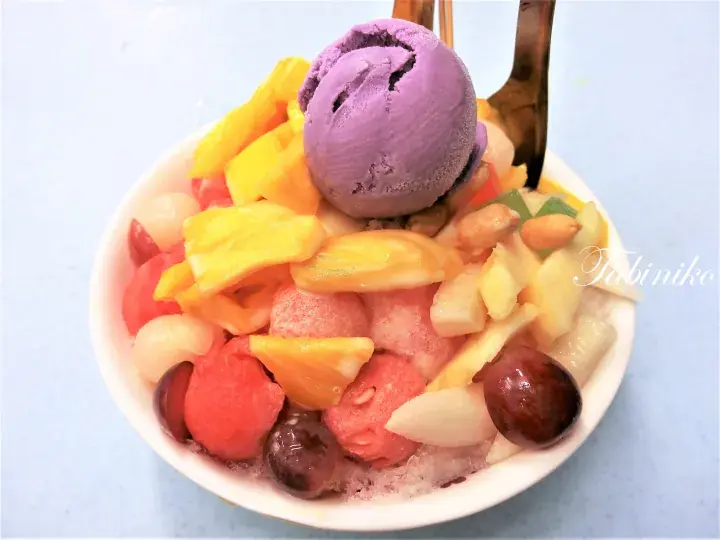 紫色アイスクリームと金色のフォークが添えられた、色とりどりのミックスフルーツデザートボウル。