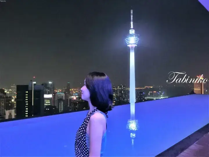 Woman at rooftop infinity pool overlooking Kuala Lumpur Tower at night.