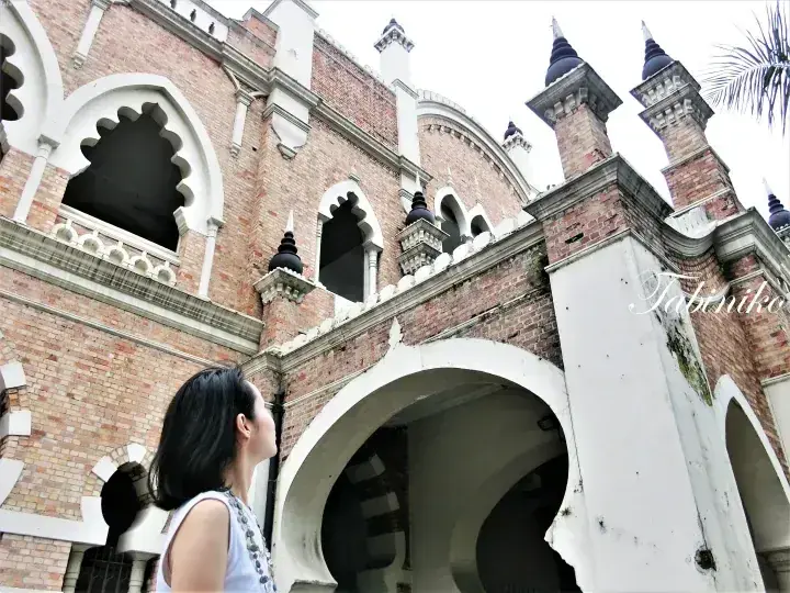 A woman gazes up at the historic brick architecture of the Sultan Abdul Samad Building in Kuala Lumpur.