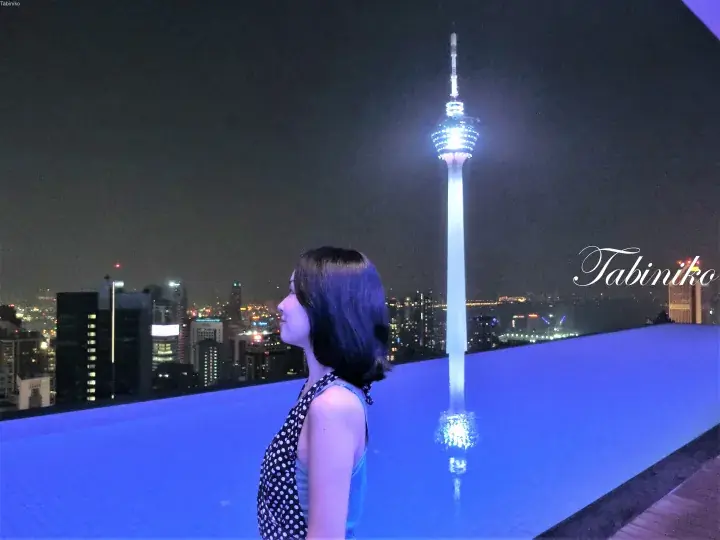 夜のカンタール・タワーを望むルーフトップのインフィニティプールでポーズをとる女性。