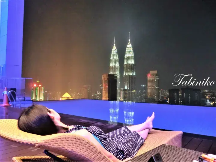 クアラルンプールのペトロナスツインタワーズを夜景に望むインフィニティプールでくつろぐ女性。