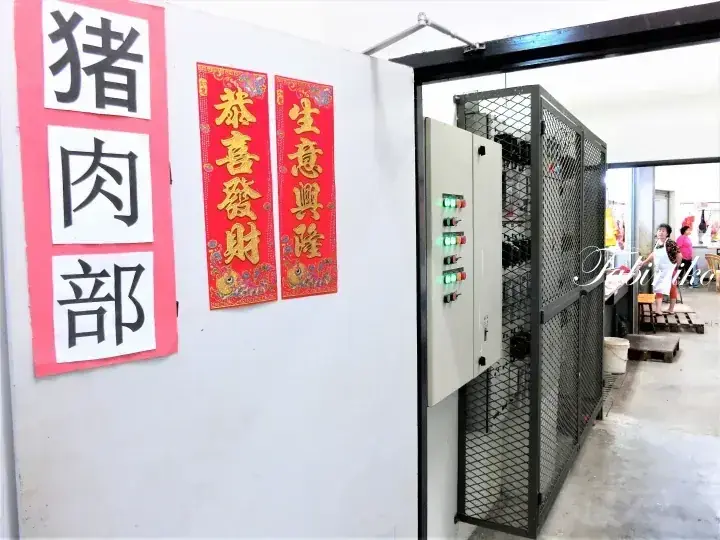 Sign reading &lsquo;Pork Department&rsquo; next to red banners and a metal cage door in a Malaysian shop.