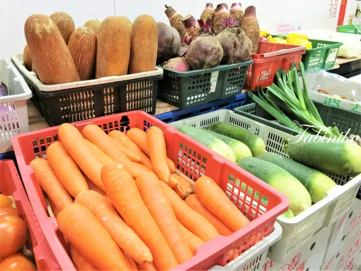 色とりどりのプラスチックケースに並べられた、新鮮な人参やキュウイ、根菜類の市場の野菜売り場。