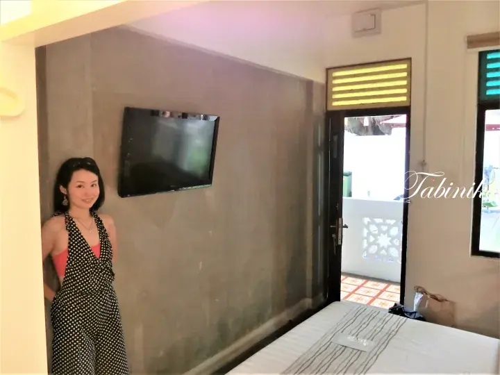 壁掛けテレビとバルコニーへの出入り口があるモダンなホテルの部屋でポーズをとる女性。