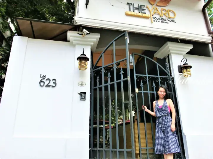 女性が入り口の門に立つ「The Yard Boutique Hotel」の外観。白い壁に「Lot 623」の番号が見える。