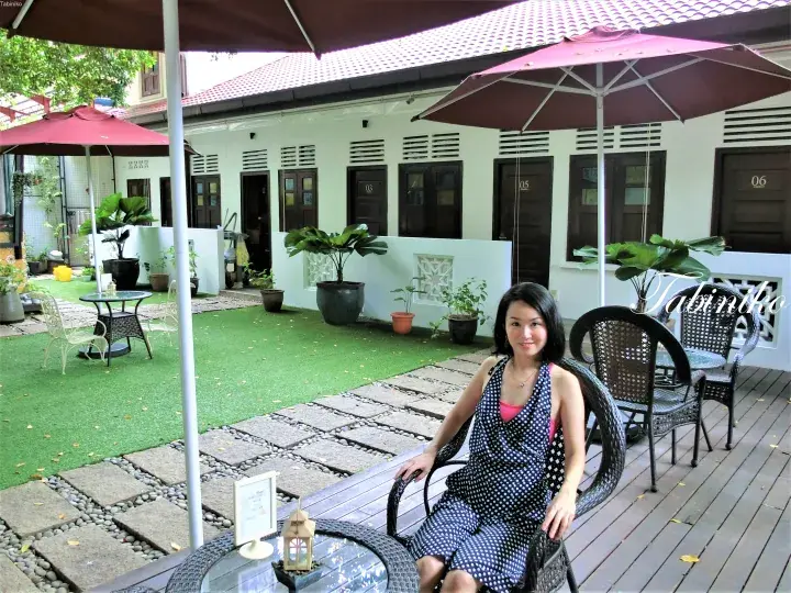 緑の芝生と日傘のあるブティックホテルの中庭で、番号付き部屋の前で座る女性。