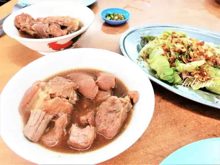 A plate of braised pork knuckle in dark gravy alongside stir-fried lettuce with garlic and a bowl of meat soup.