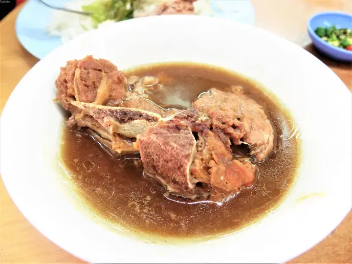 白い器に盛られた、濃厚な褐色のスープと柔らかい肉が特徴の骨付きスープ料理。