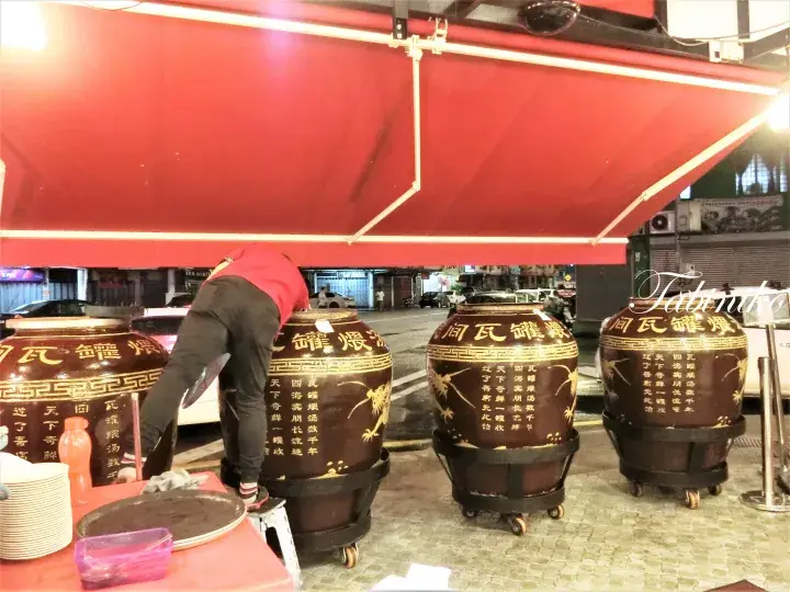 赤い屋根の下で大きな陶器の壺を扱う作業員。