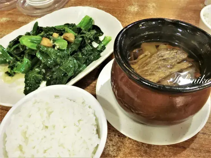 A clay pot of herbal soup with rice and stir-fried greens on a wooden table