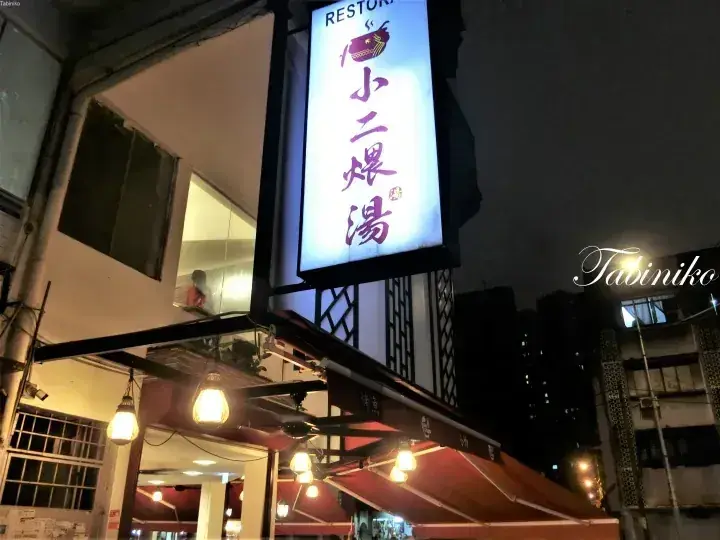 Illuminated vertical sign for Xiao Er Soup restaurant at night, featuring Chinese characters and a fish logo.