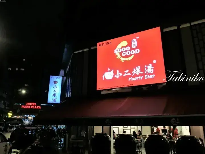Sooo Good Hearty Soup restaurant sign at night in Kuala Lumpur, with Hotel Pudu Plaza visible in the background.