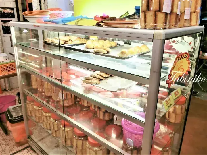 Glass display cabinet filled with jars of kuih and trays of pastries at a Malaysian bakery.