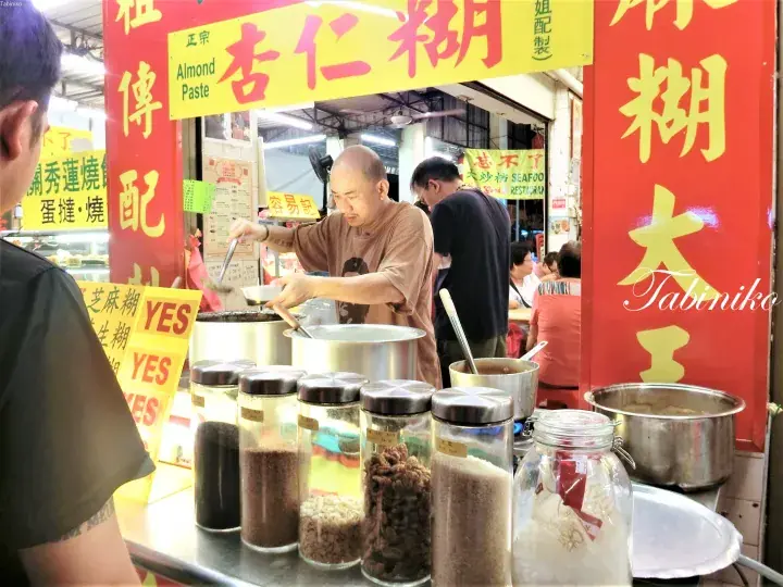 マレーシアの屋台で杏仁糊を調理する店員と、並べられた具材の瓶。