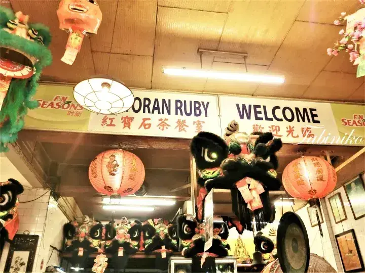 Interior of Gran Ruby restaurant featuring traditional Chinese lion dance heads, red lanterns, and a sign reading ‘Gran Ruby 紅寶石茶餐室’.