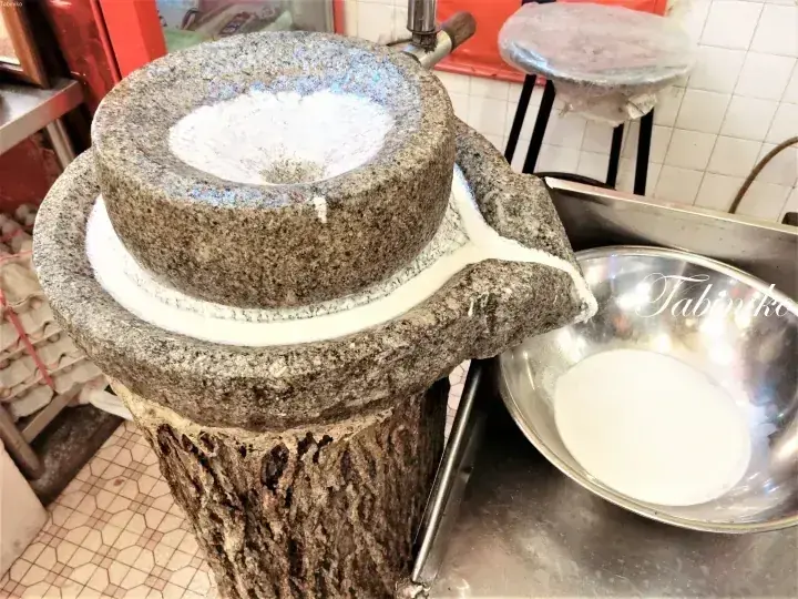 Traditional stone mill grinding white paste, likely for making traditional Malaysian desserts.
