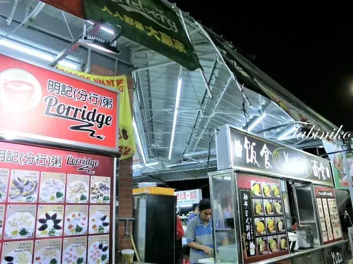 Night view of a food stall with a red Porridge sign and menu board displaying various dishes.