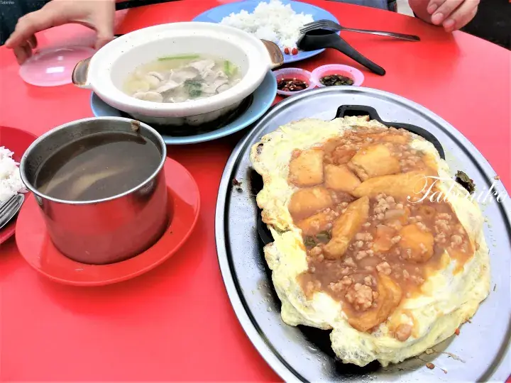 赤いテーブルの上に並ぶ、挽肉とじゃがいもを乗せた鉄板オムレツ、スープ、ご飯の马来西亚料理。